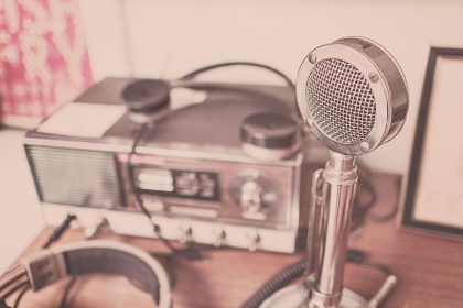 Microfone vintage, aparelho de rádio e fones de ouvido sobre uma mesa de madeira.