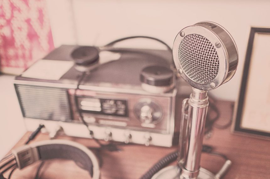 Microfone vintage, aparelho de rádio e fones de ouvido sobre uma mesa de madeira.