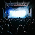 Grande público acompanha um show ao vivo em um festival de música ao ar livre, sob luzes coloridas.