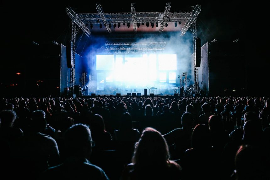 Grande público acompanha um show ao vivo em um festival de música ao ar livre, sob luzes coloridas.