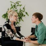 Duas mulheres sentadas conversam em um ambiente interno, em uma interação de apoio e acolhimento.