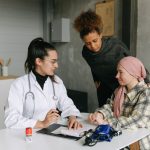 Paciente conversa com um médico e uma pessoa próxima em casa durante um momento de acompanhamento e apoio.