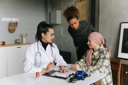 Paciente conversa com um médico e uma pessoa próxima em casa durante um momento de acompanhamento e apoio.