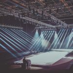 Palco interno amplo com estrutura de iluminação dramática preparado para uma apresentação musical.