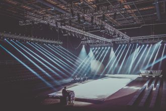 Palco interno amplo com estrutura de iluminação dramática preparado para uma apresentação musical.