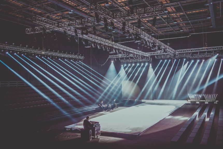 Palco interno amplo com estrutura de iluminação dramática preparado para uma apresentação musical.