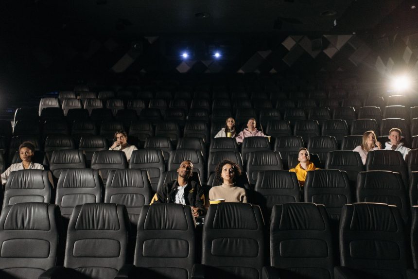 Público diversificado sentado em uma sala de cinema pouco iluminada durante uma sessão